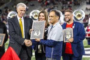 Gordon Henderson (left) presents a plaque acknowledging all past and present directors of the Pride of Arizona to University of Arizona President Suresh Garimella (right) and Vice President and Director of Athletics Desirée Reid-Francois (center).